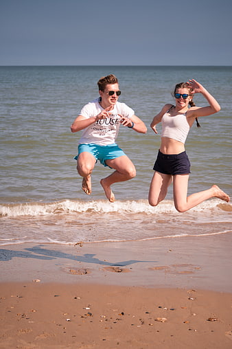 Happy young couple jumping on sandy beach in summer