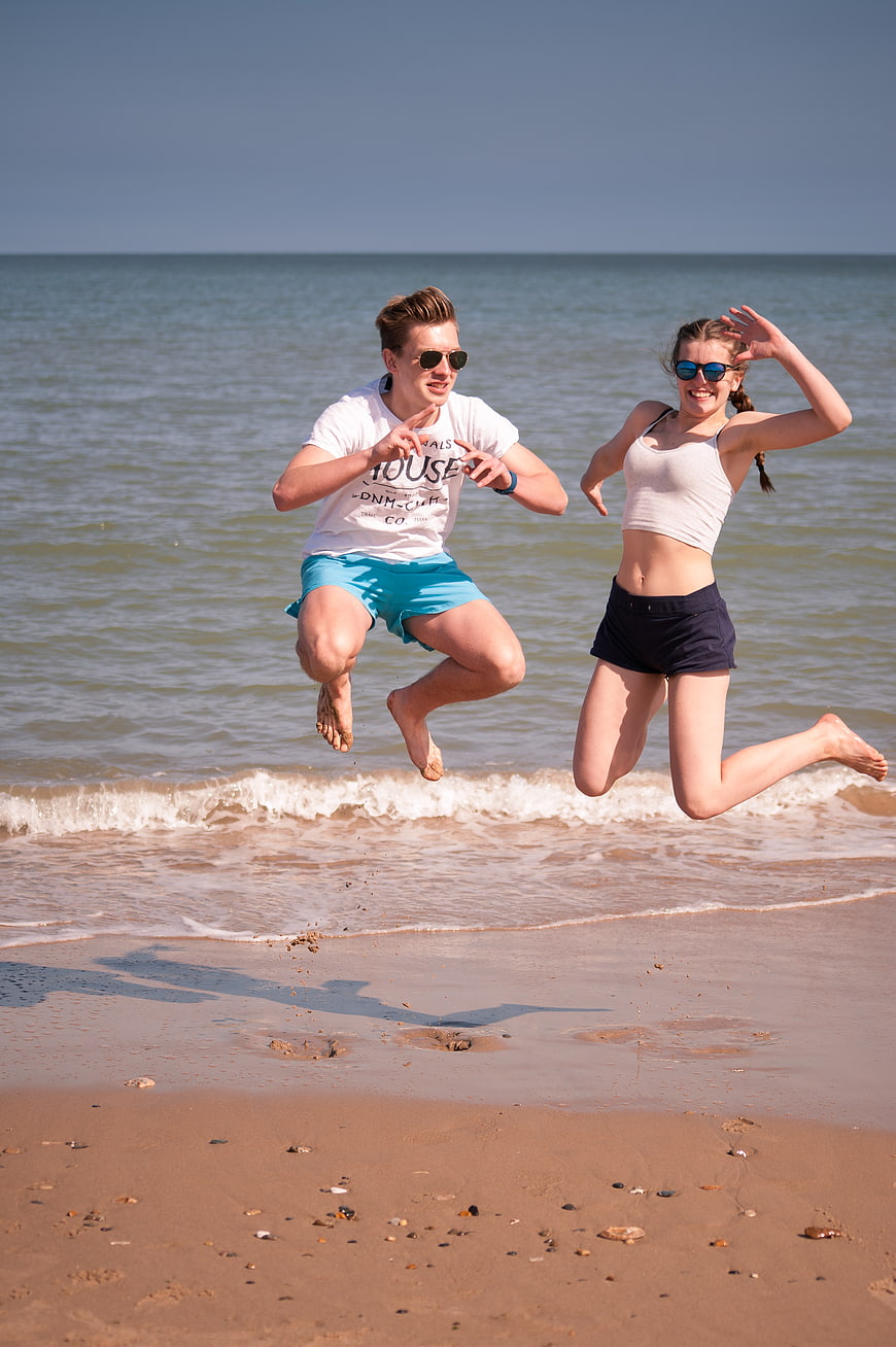 Happy young couple jumping on sandy beach in summer