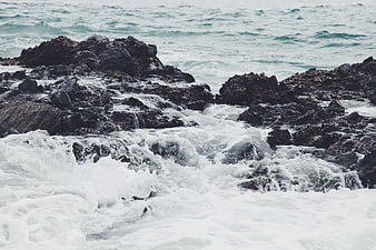 Rough ocean waves crashing against dark rocky coastline