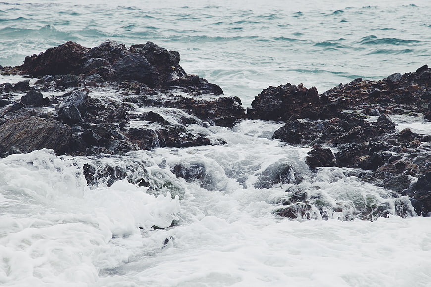 Rough ocean waves crashing against dark rocky coastline
