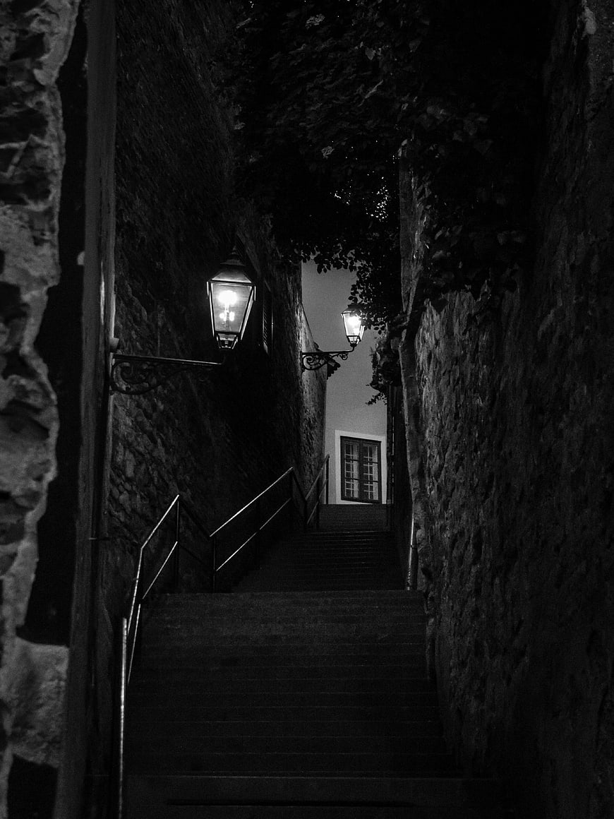 Dark narrow stone staircase with vintage lamps at night