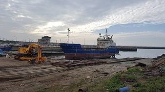 Blue cargo ship docked at industrial harbor with excavator