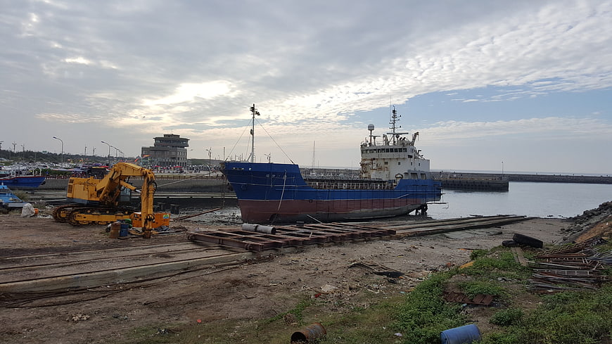 Blue cargo ship docked at industrial harbor with excavator