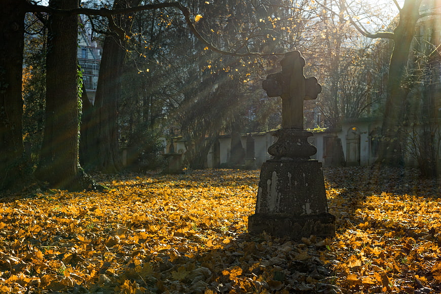 Sunlit Stone Cross in Autumn Cemetery with Golden Leaves