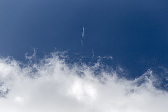 Airplane contrail in deep blue sky with white clouds