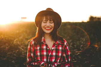 Happy woman in plaid shirt and hat smiling in golden sunlight
