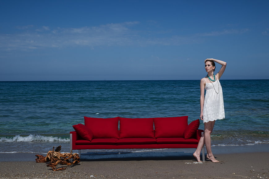 Woman in white dress standing next to red sofa on beach