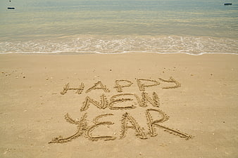 Happy New Year written in sand on a calm beach shoreline