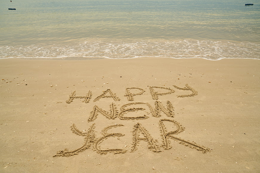 Happy New Year written in sand on a calm beach shoreline