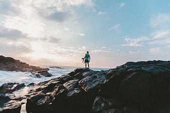 Man standing on rocky coast looking at ocean sunset