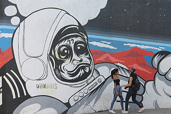 Two women walking past large astronaut monkey street art mural