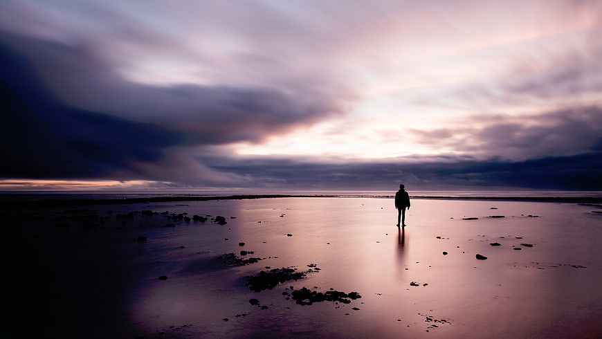 Silhouette of person standing on wet beach at sunset