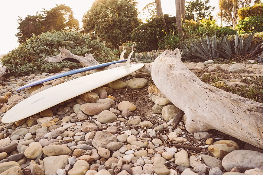 White surfboard resting on pebbles near driftwood
