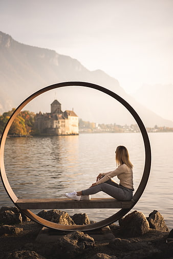 Woman sitting in circular frame overlooking Swiss castle lake