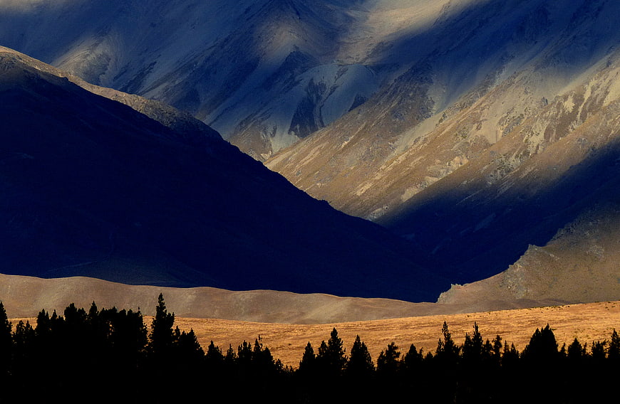 Dramatic Mountain Landscape with Golden Sunlight and Silhouetted Trees