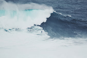 Surfer riding massive ocean wave with crashing whitewater