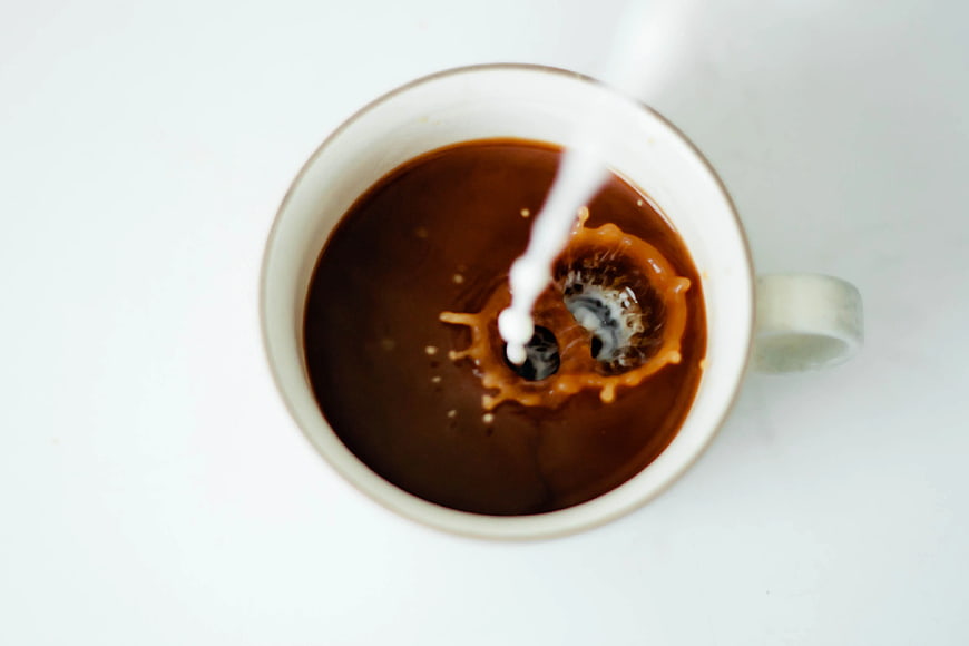 Top View of Milk Splashing into Black Coffee Cup