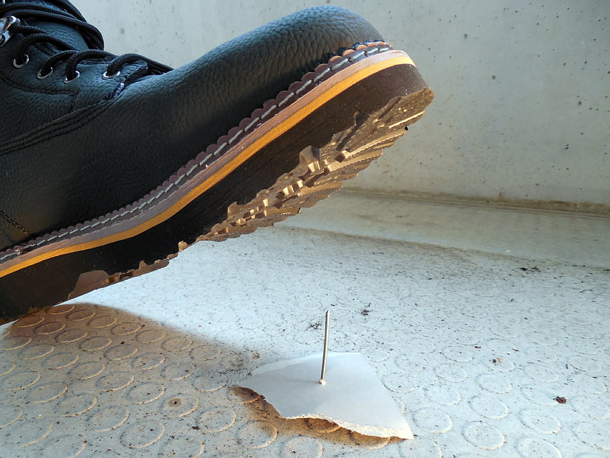 Black work boot stepping over a nail on concrete floor