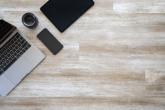 Flat lay of laptop, tablet, smartphone, and camera lens on wooden desk