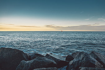 Serene Ocean Sunset with Distant Sailboat and Foreground Rocks