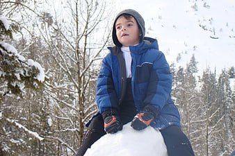 Young boy sitting on snowball in winter forest