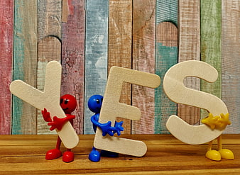 Colorful figures holding wooden YES letters on rustic background
