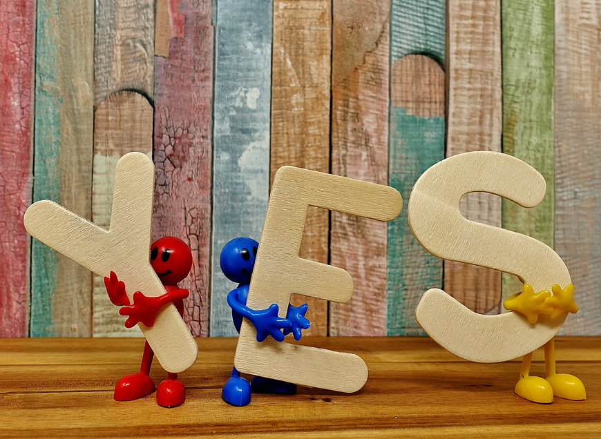 Colorful figures holding wooden YES letters on rustic background
