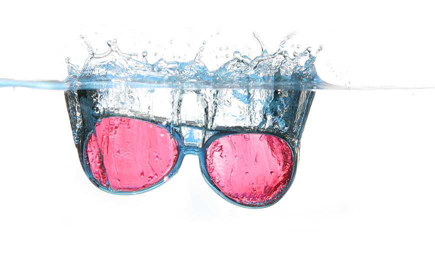 Pink sunglasses splashing into water on white background