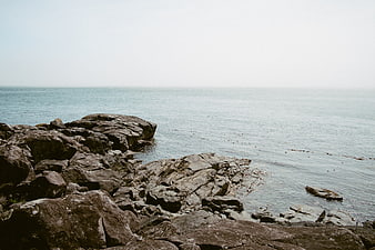 Serene Rocky Coastline with Calm Ocean and Misty Sky