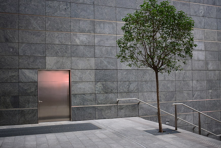 Modern gray stone wall with metal door and tree