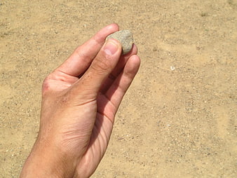 Hand holding small stone against sandy background