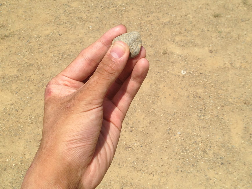 Hand holding small stone against sandy background