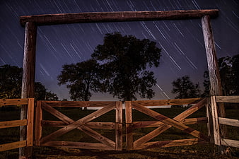 Star trails over rustic wooden gate and trees at night