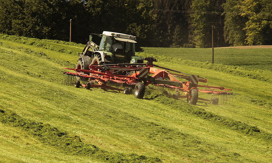Tractor Raking Hay in Green Meadow Field