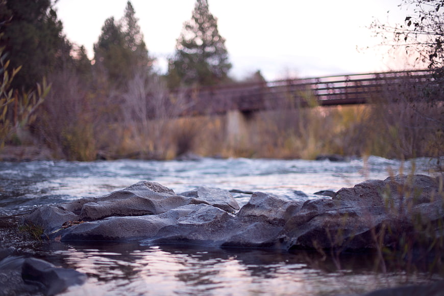 Flowing river with rocks and blurred bridge background