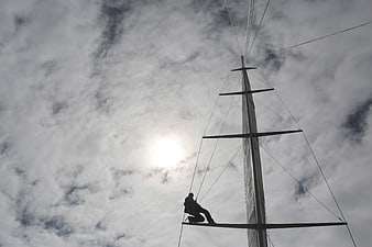Silhouette of sailor climbing sailboat mast against cloudy sky