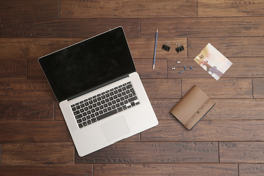 Flat lay of laptop, notebook, and office supplies on wooden desk