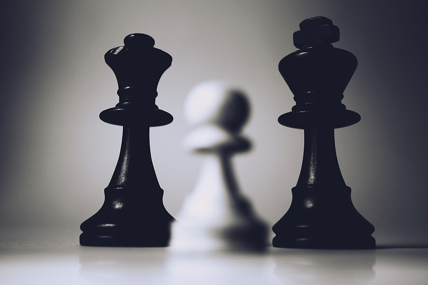 Black Chess Queens Flanking Blurred White Pawn