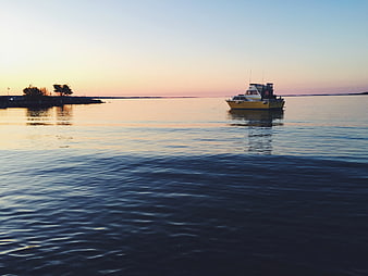 Yellow boat anchored on calm water at sunset