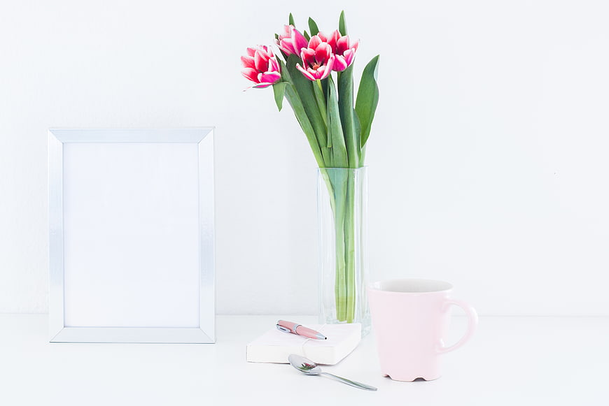 Minimalist white desk with pink tulips, photo frame, and coffee cup