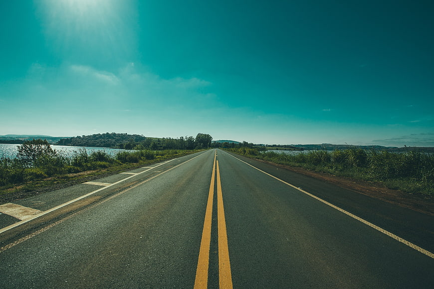 Empty asphalt road stretching toward horizon with lake and hills