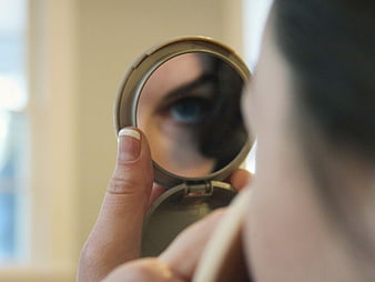 Woman applying eye makeup looking in compact mirror