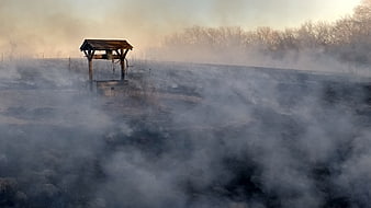 Rural wooden well structure surrounded by thick smoke in a burnt field
