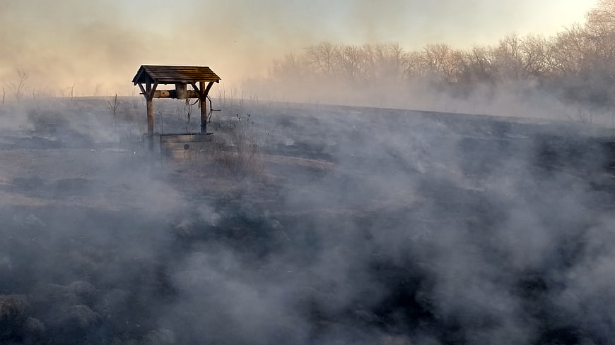 Rural wooden well structure surrounded by thick smoke in a burnt field