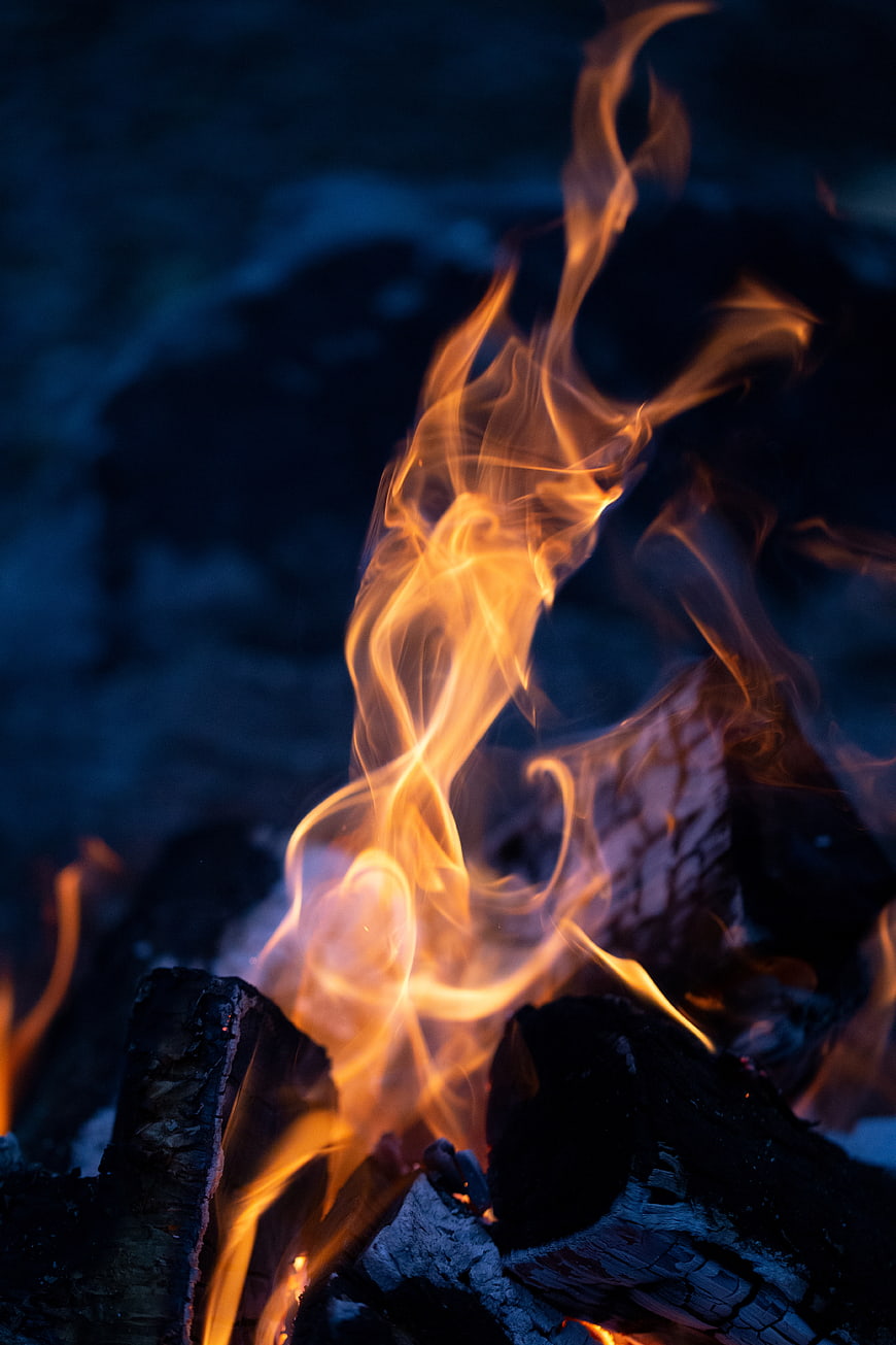 Close-up of vibrant orange flames burning on charred wood at night