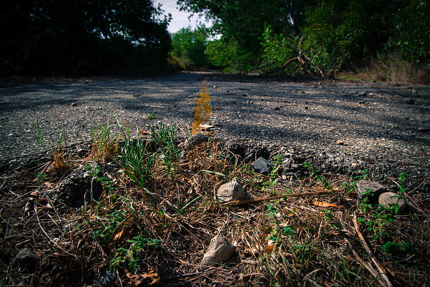 Overgrown asphalt road with yellow line and weeds
