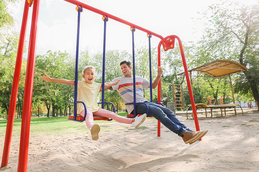 Happy father and daughter swinging together in a sunny park