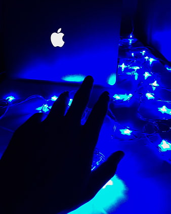Silhouette of hand reaching toward glowing blue star lights and laptop