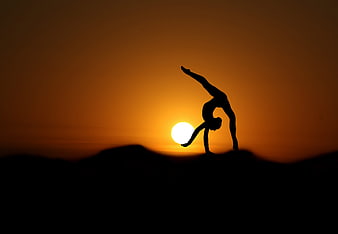Silhouette of a woman performing a backbend yoga pose at sunset