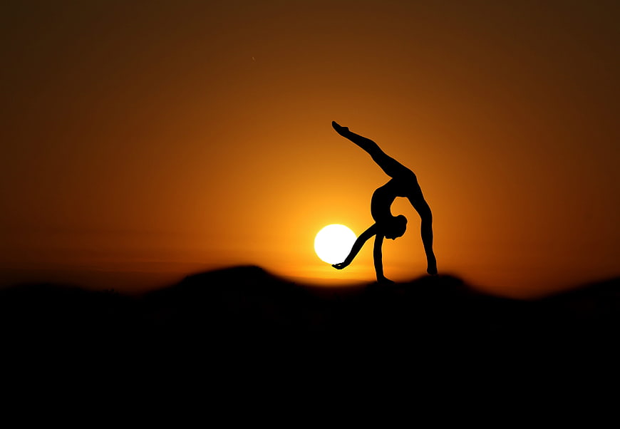 Silhouette of a woman performing a backbend yoga pose at sunset